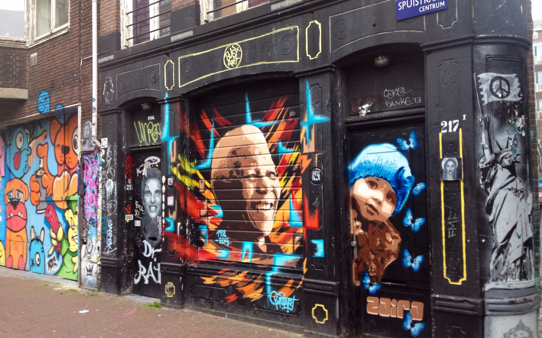 Street art murals on a building in Amsterdam's Spuistraat, featuring colorful portraits and graffiti.
