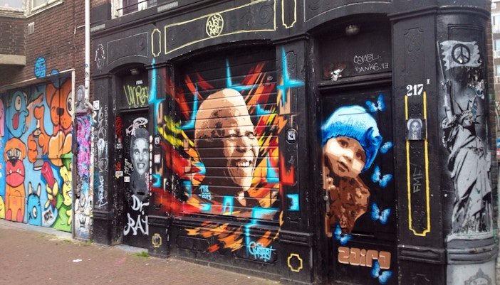 Street art murals on a building in Amsterdam's Spuistraat, featuring colorful portraits and graffiti.