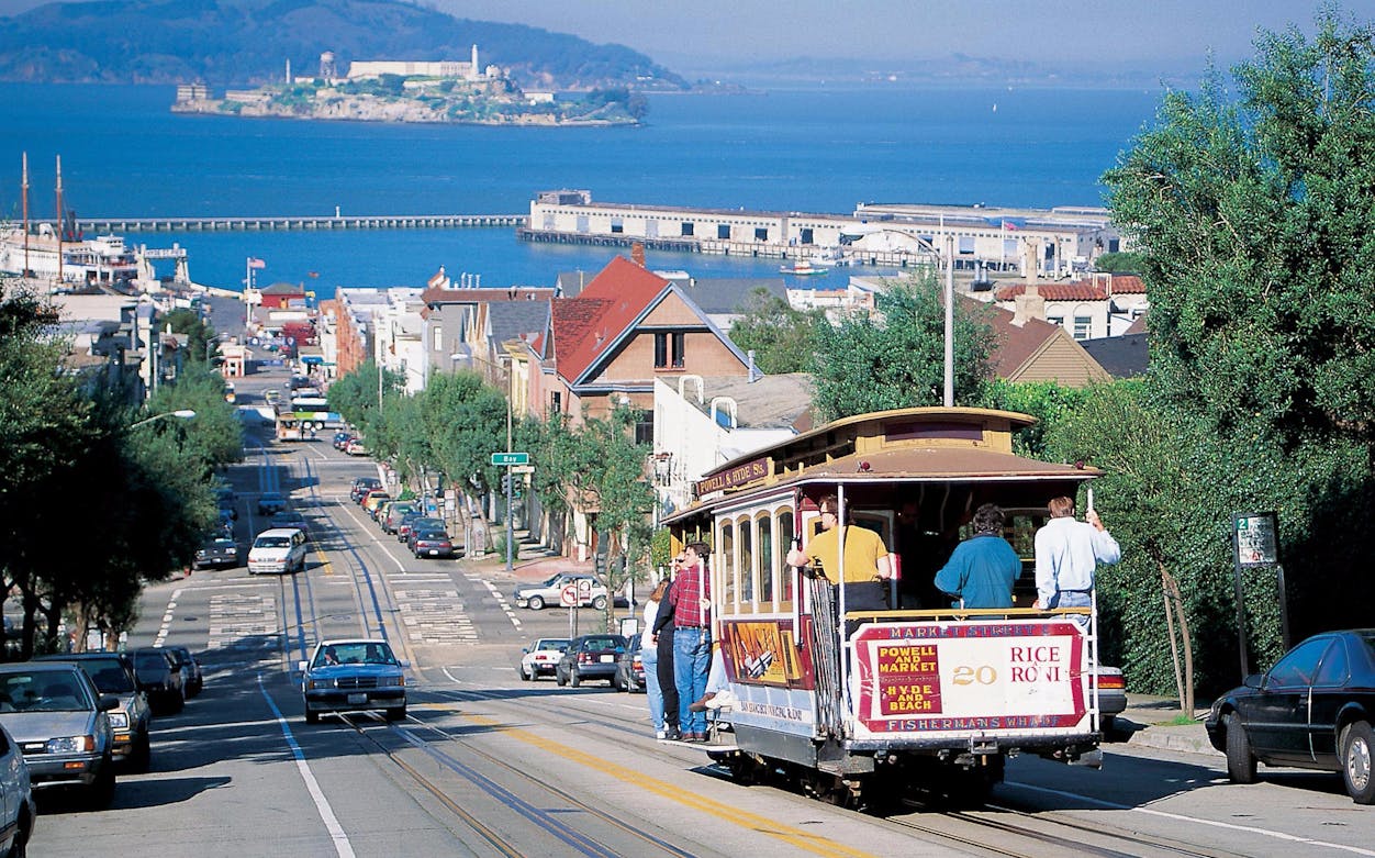 San Francisco cable car on a hill with Alcatraz Island in the background.
