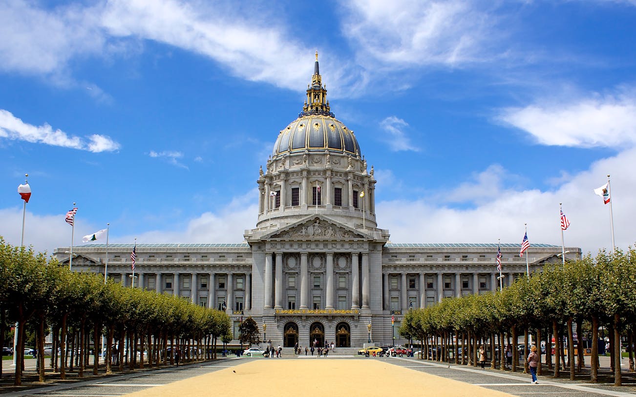 San Francisco City Hall with flags and trees in Civic Center Plaza.