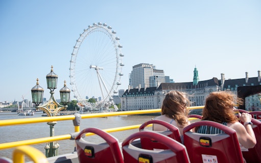 Open-top bus tour in London passing the London Eye and River Thames.
