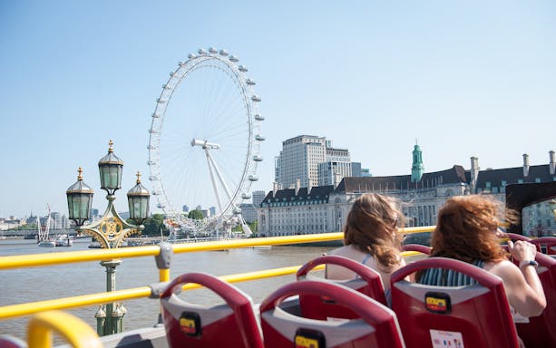 Open-top bus tour in London passing the London Eye and River Thames.