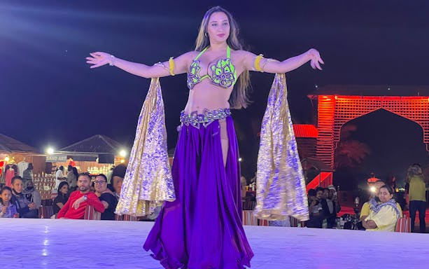 Dancer performing at desert safari with audience in background.