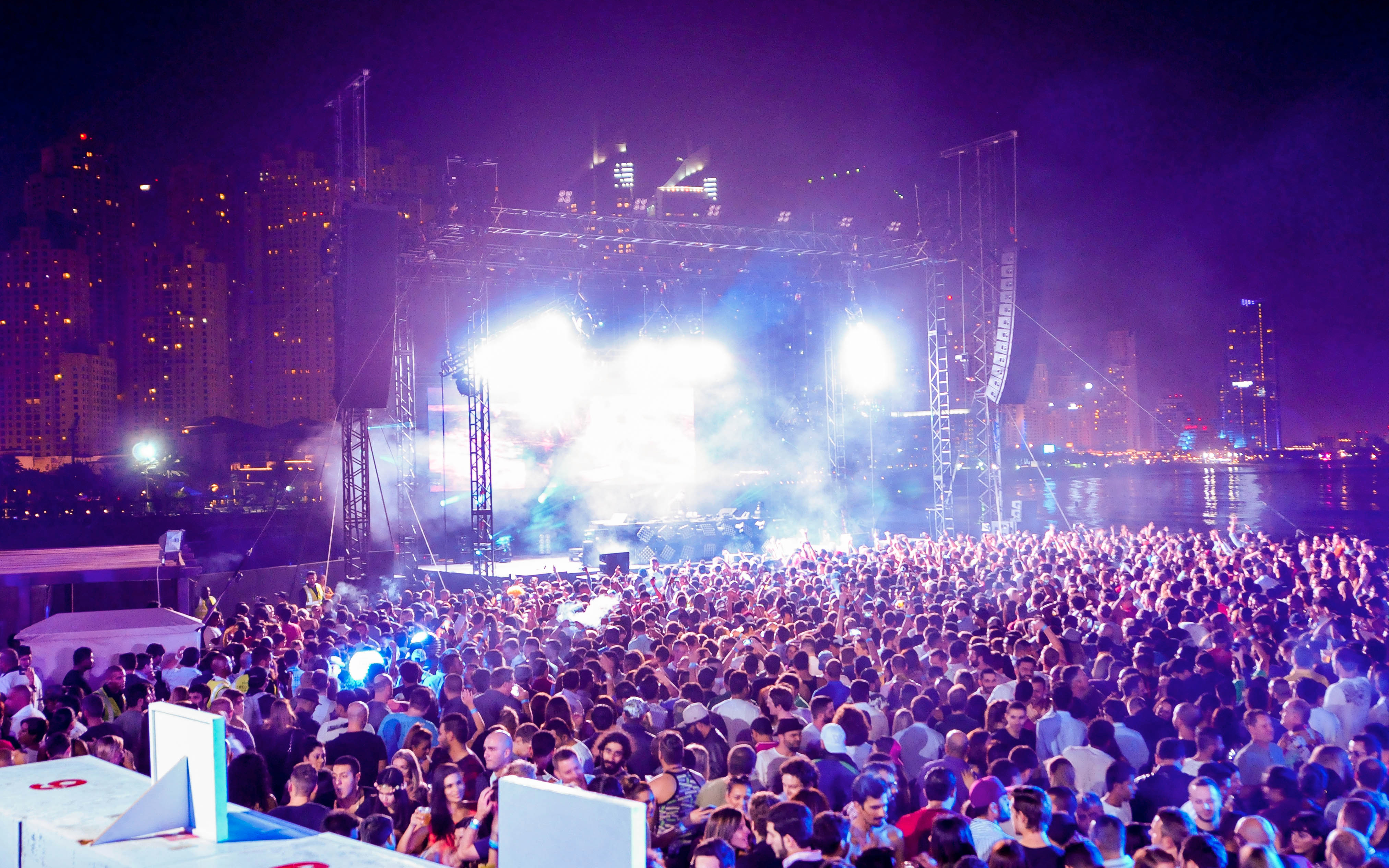 Crowd enjoying DXBeach music festival at night with city skyline in the background.