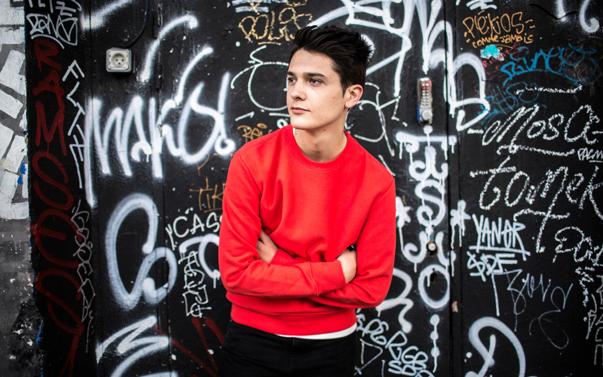 Man in red sweater standing against graffiti wall at DXBeach event.