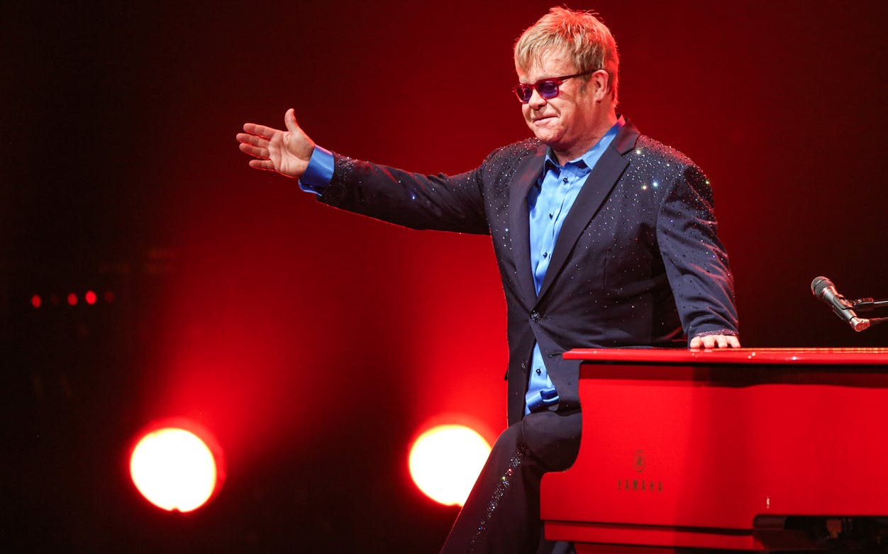 Performer at red piano on stage with vibrant lighting.