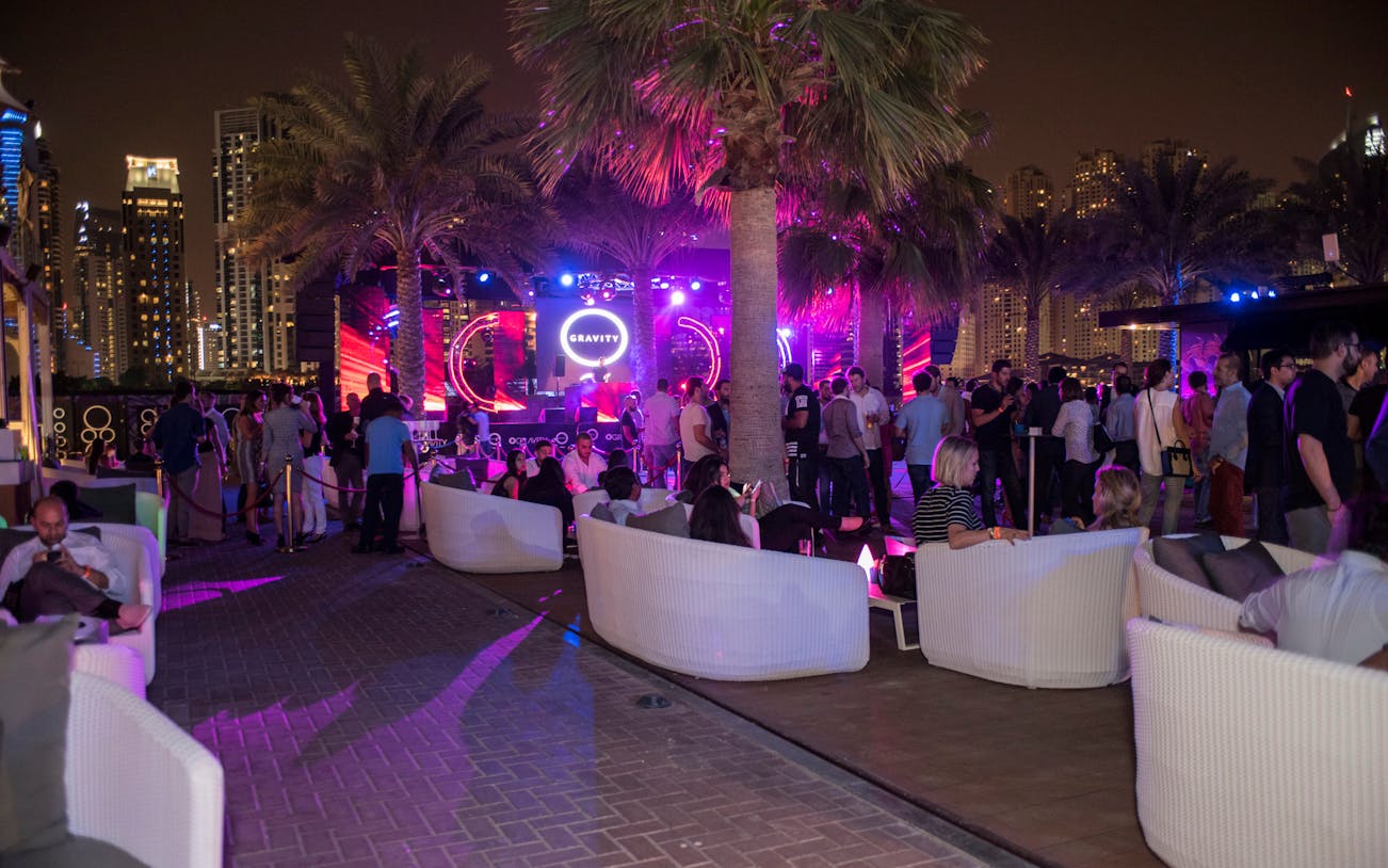 Outdoor night event with a crowd at a Dubai venue, featuring a lit stage and palm trees.