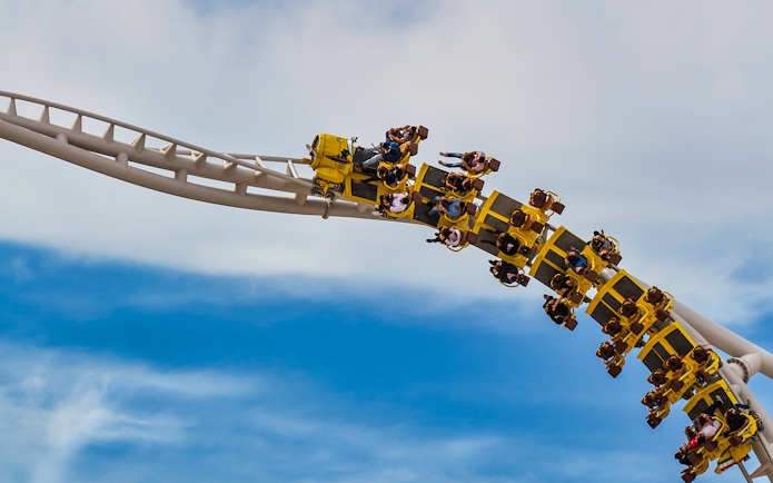 Roller coaster at Ferrari World Abu Dhabi with riders on a loop against blue sky.