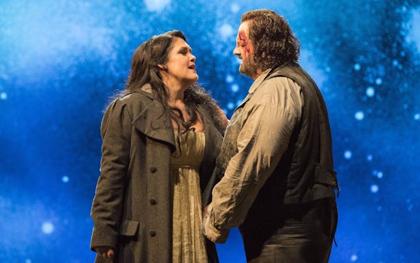 Opera performers in a dramatic scene from Tosca against a starry backdrop.