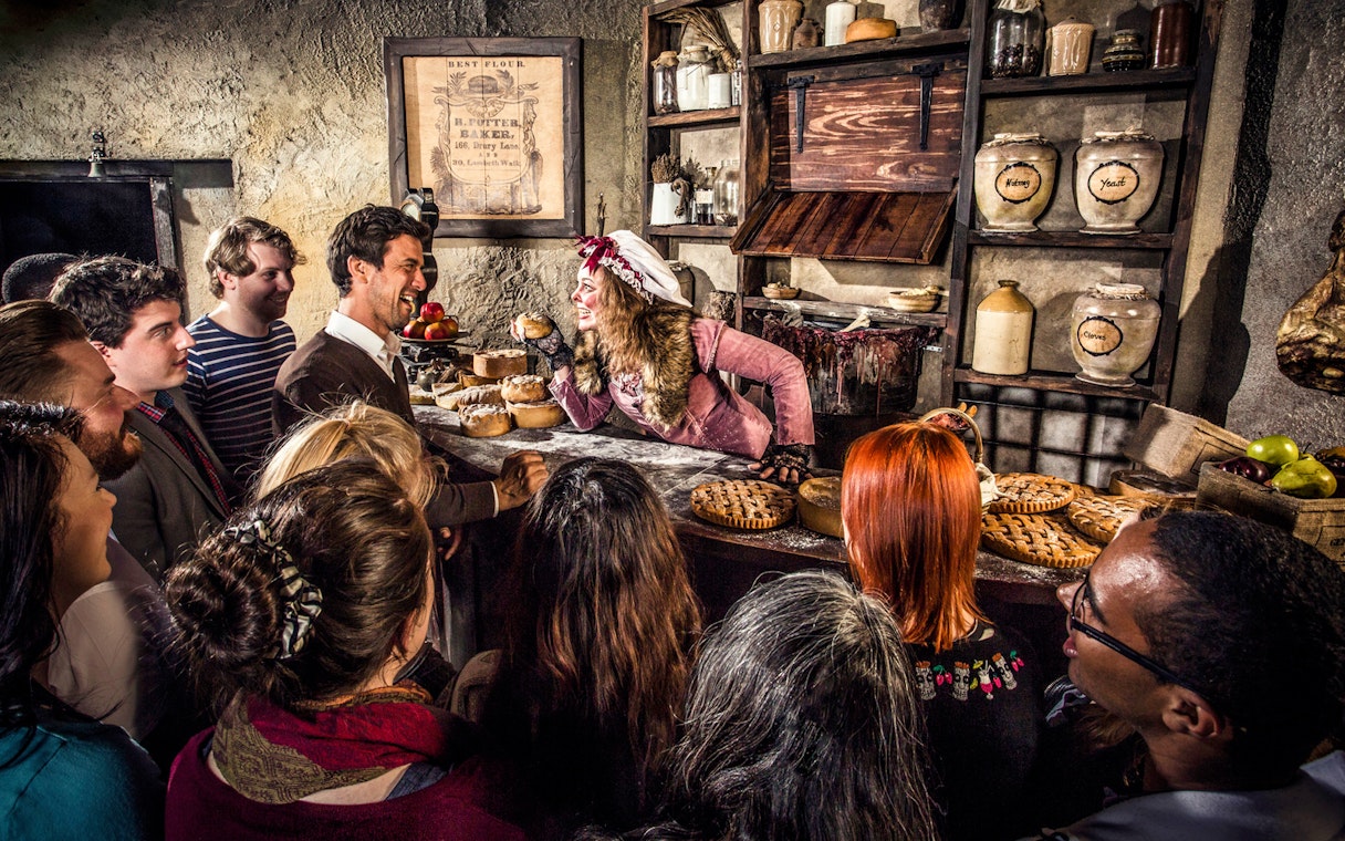 Visitors interact with a costumed performer in a historical bakery setting at the London Dungeon.