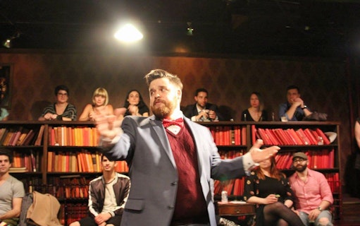 Performer in a suit gestures during a Drunk Shakespeare show with audience in background.