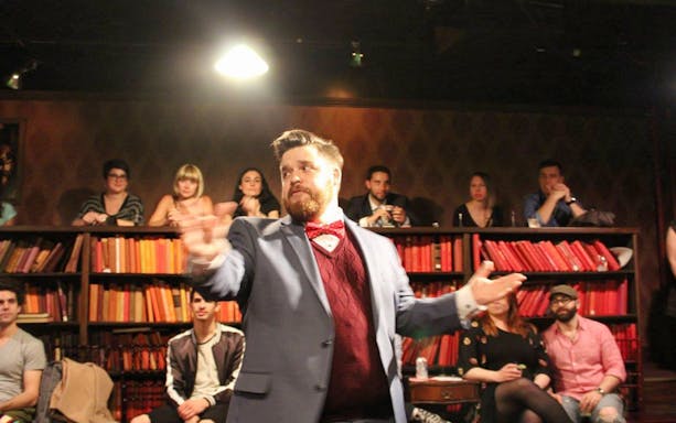 Performer in a suit gestures during a Drunk Shakespeare show with audience in background.