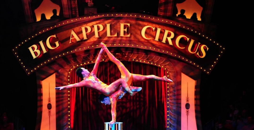 Acrobats performing at Big Apple Circus under illuminated marquee.