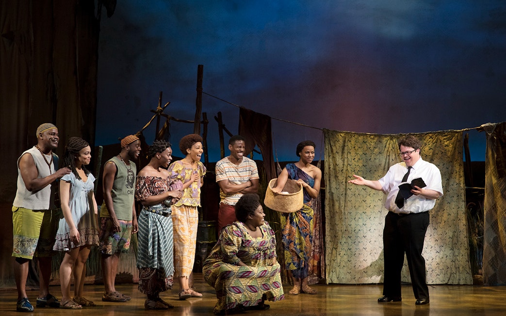 Cast performing a scene from "The Book of Mormon" musical on stage.