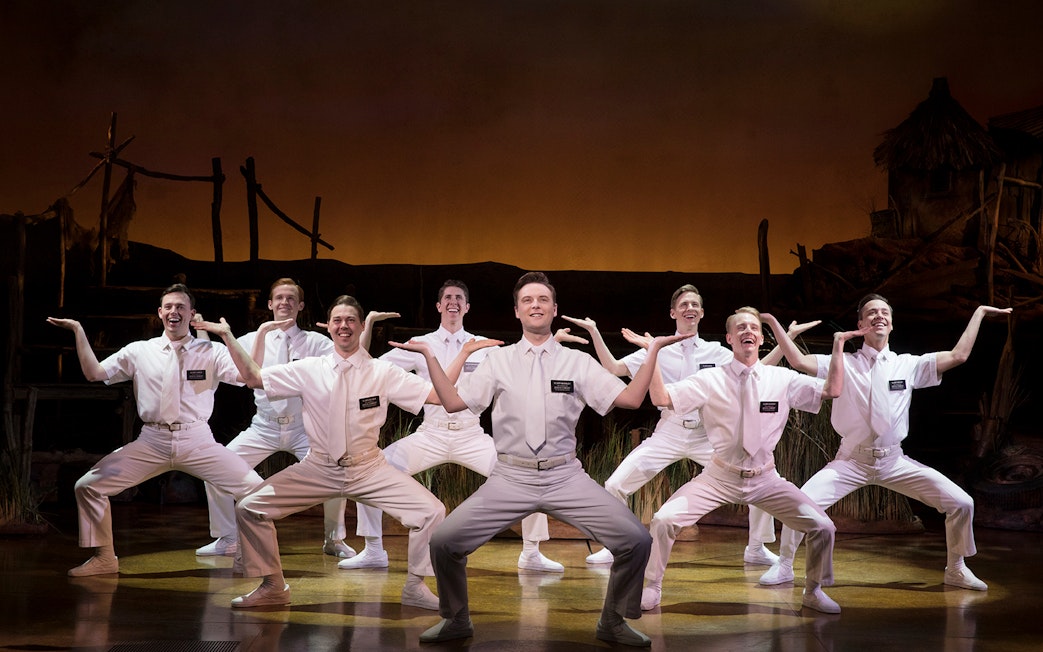 Performers in white costumes on stage during The Book of Mormon musical.