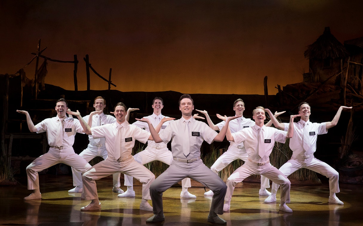 Performers in white costumes on stage during The Book of Mormon musical.