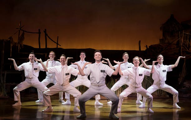 Performers in white costumes on stage during The Book of Mormon musical.