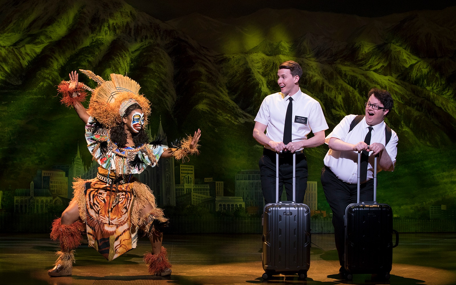 Performers in "The Book of Mormon" musical scene with vibrant costumes and props.