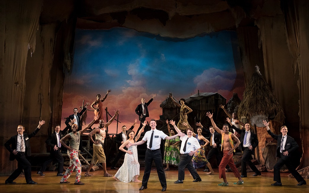 Cast performing a scene from The Book of Mormon musical on stage.