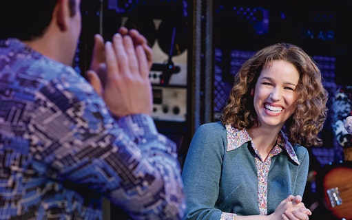 Performer smiling during "Beautiful: The Carole King Musical" scene.