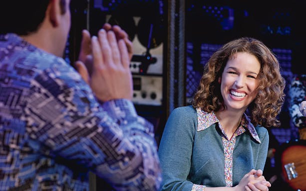 Performer smiling during "Beautiful: The Carole King Musical" scene.
