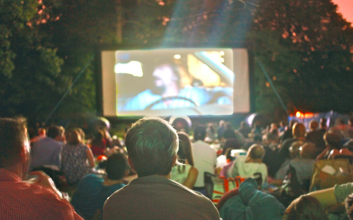 Crowd watching a movie at an outdoor cinema in a park at dusk.
