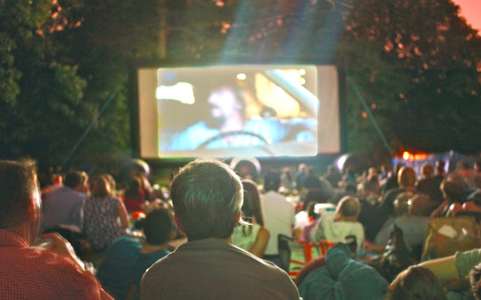Crowd watching a movie at an outdoor cinema in a park at dusk.