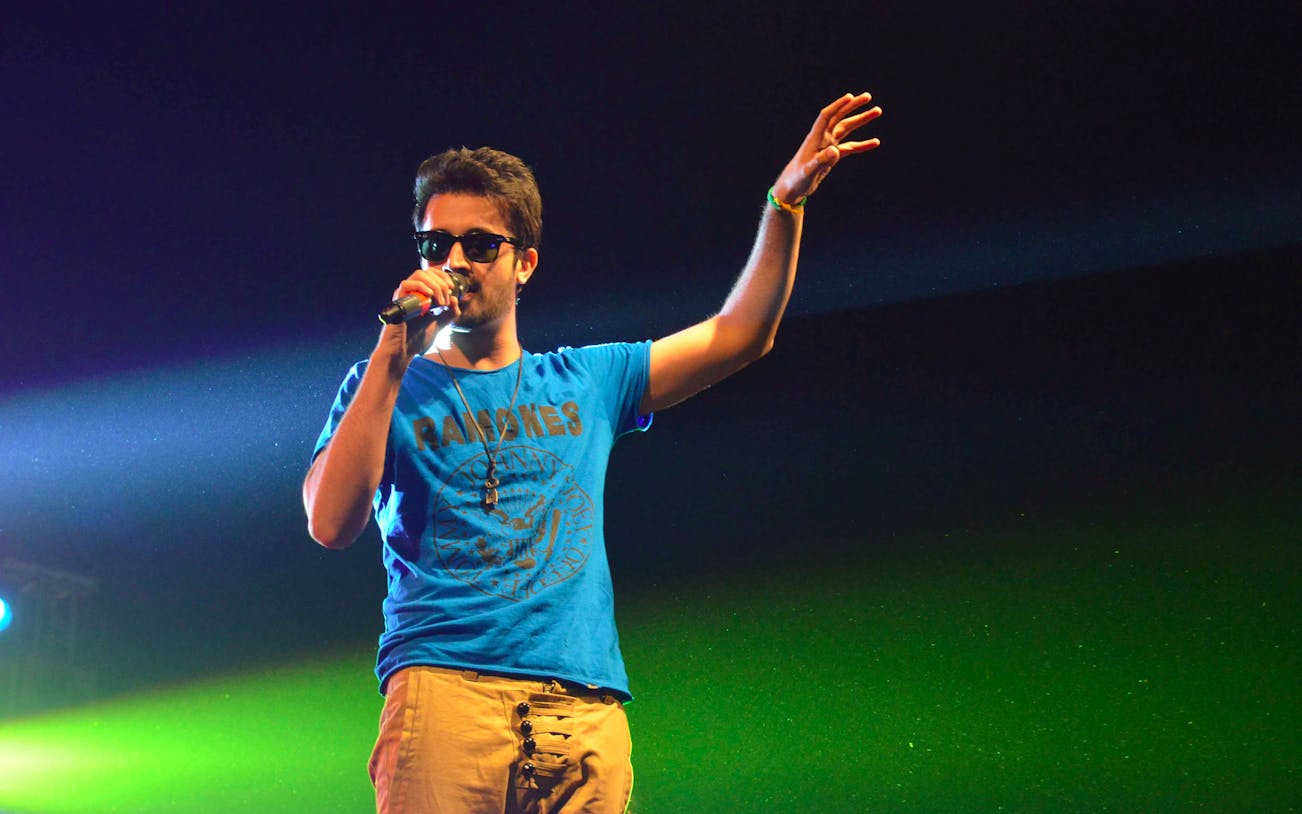 Singer performing live on stage with microphone, vibrant lighting.