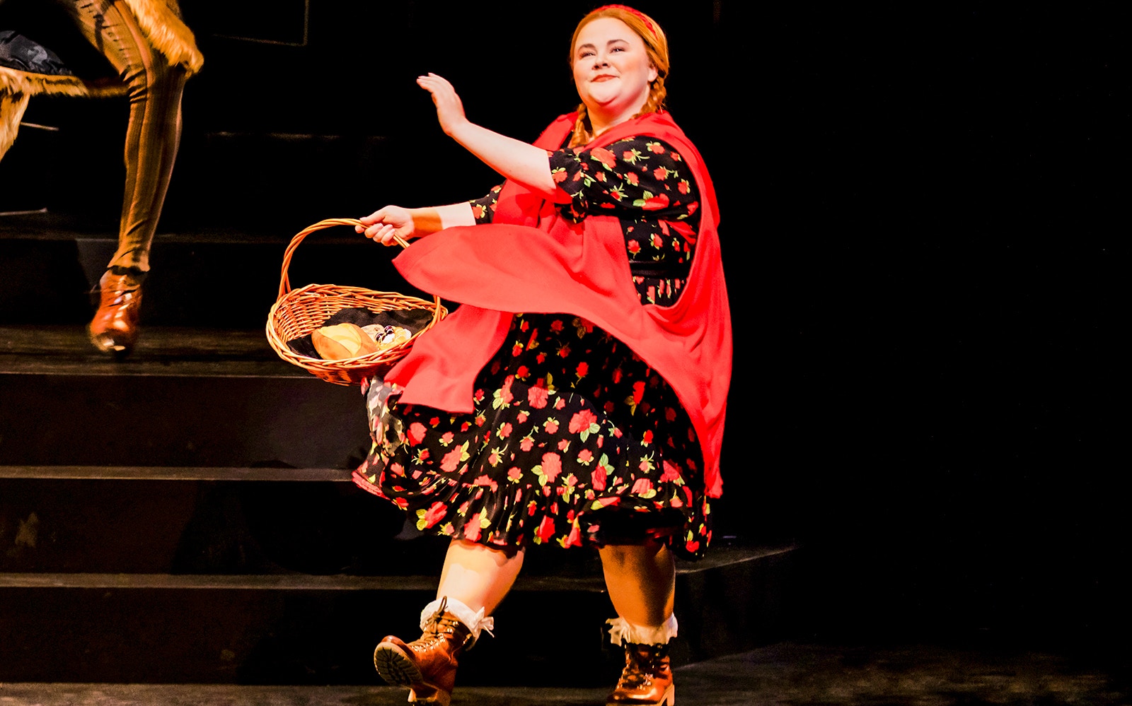 Performer in red cape holding basket on stage during "Into The Woods" musical.