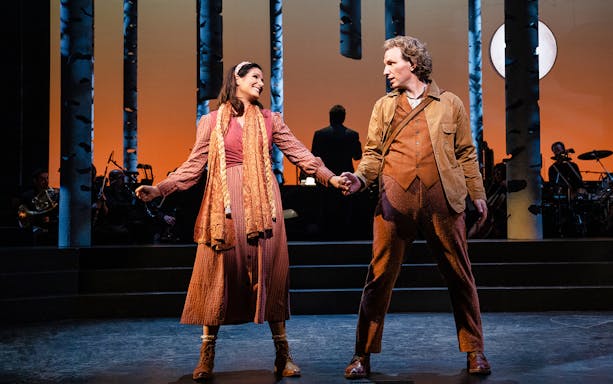 Actors performing on stage in "Into The Woods" musical with forest backdrop.