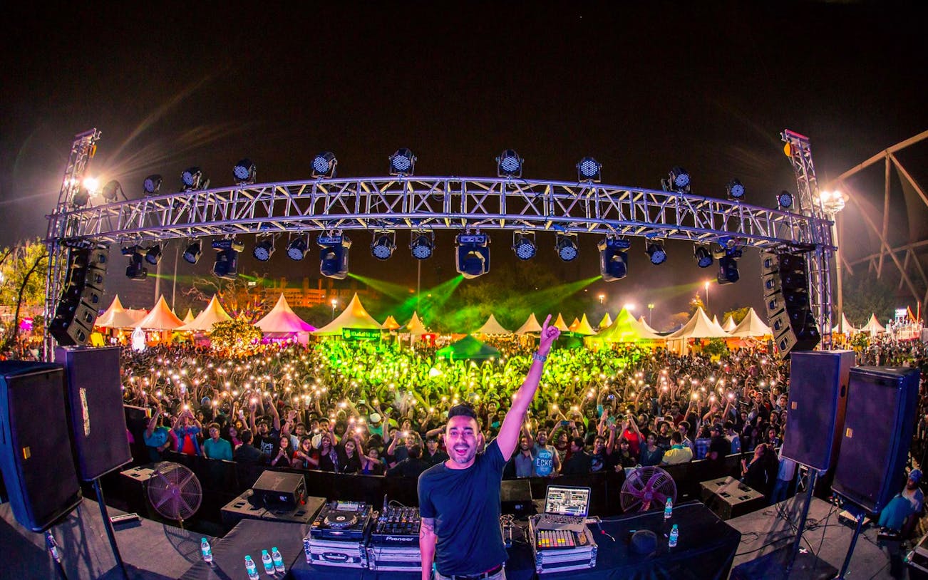 DJ performing live at an outdoor concert in Dubai with a large crowd and vibrant lights.