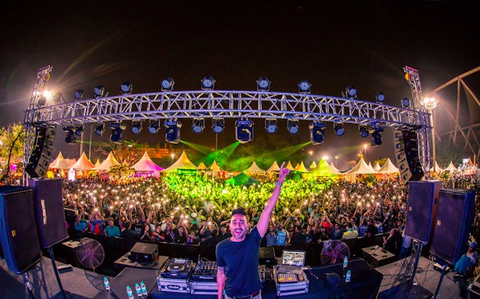 DJ performing live at an outdoor concert in Dubai with a large crowd and vibrant lights.