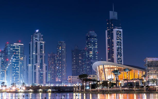 Dubai skyline at night with illuminated skyscrapers and Dubai Opera near Burj Khalifa.