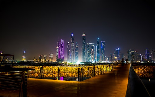 Dubai skyline at night with illuminated skyscrapers viewed from a boardwalk, part of Dubai City Tour & Burj Khalifa Tickets Combo.