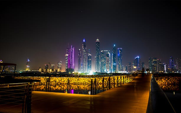 Dubai skyline at night with illuminated skyscrapers viewed from a boardwalk, part of Dubai City Tour & Burj Khalifa Tickets Combo.